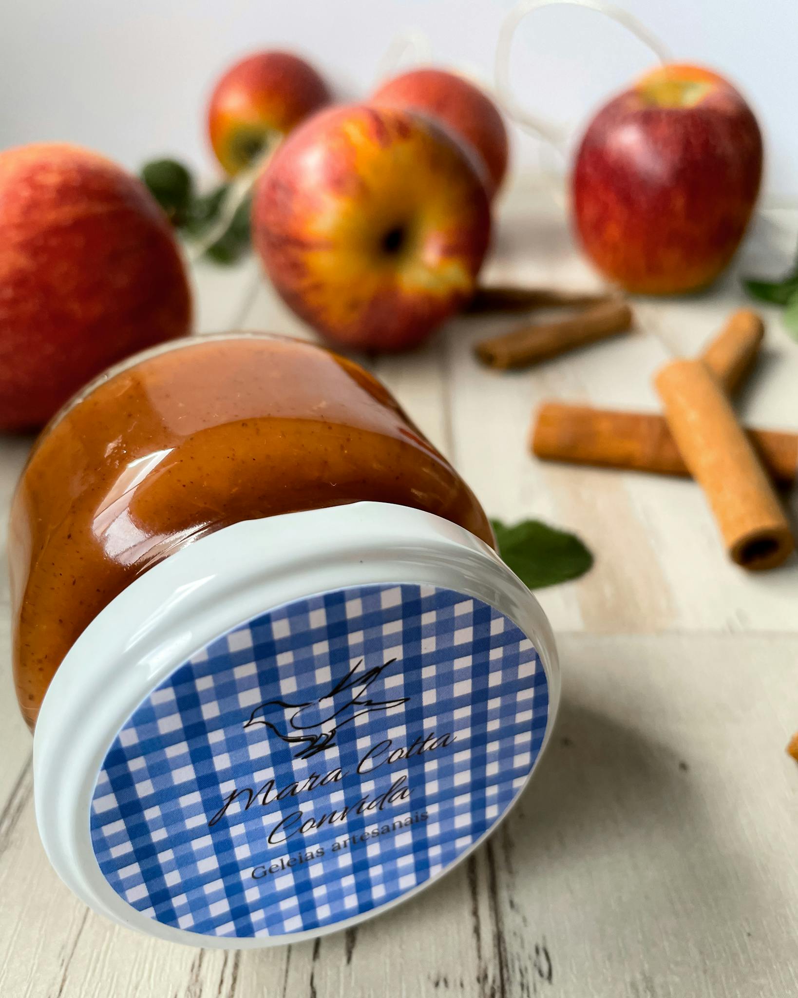 Close-up of apple cinnamon jam in jar with fresh apples and cinnamon stick on wood.