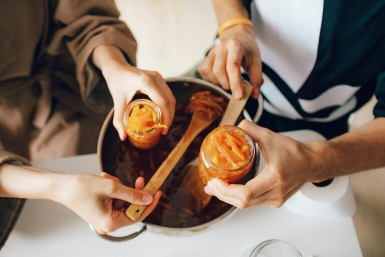 Hands making homemade orange jam, filling jars over a kitchen counter.