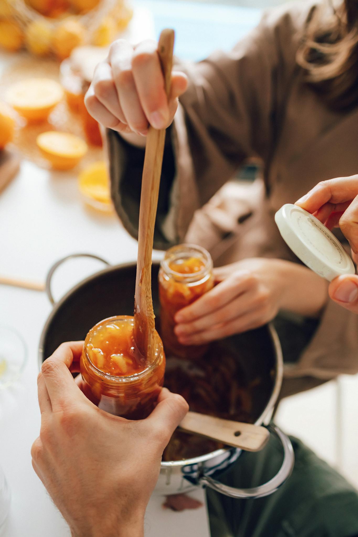 Hands preparing homemade jam in glass jars. Traditional kitchen setting.