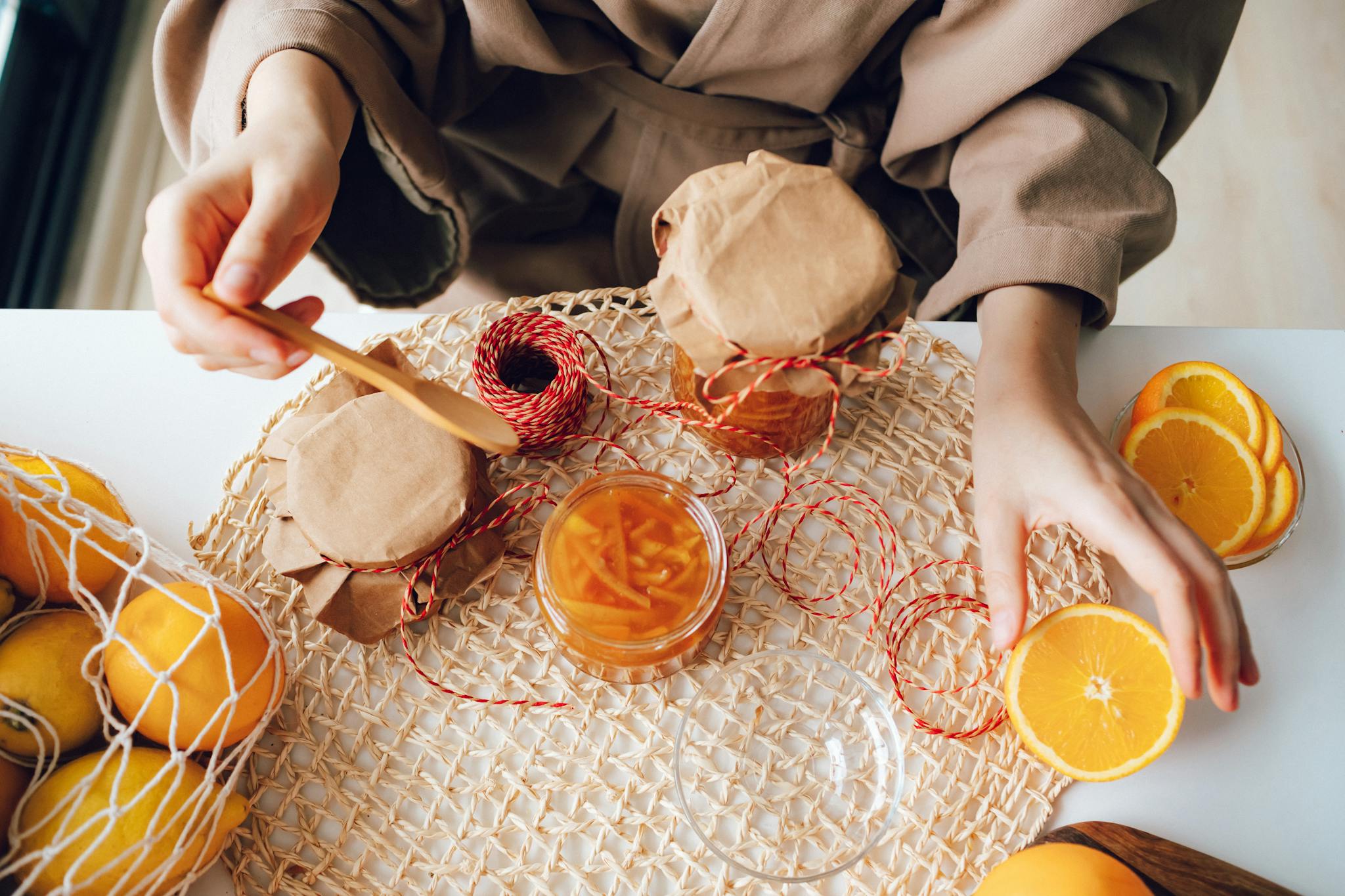 Hands preparing homemade orange marmalade with fresh oranges and jars.