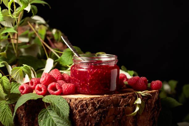 Jar of raspberry jam and fresh berries with leaves on a pine stump. copy space.