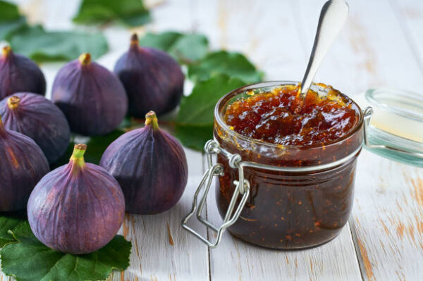 Glass jar of figs jam with fresh figs on a white wooden table.