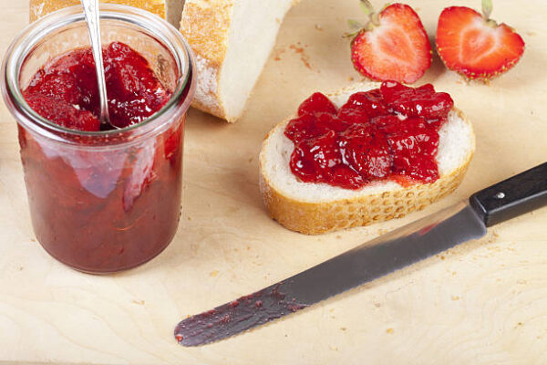 Homemade strawberry jam on white bread on a wooden board
