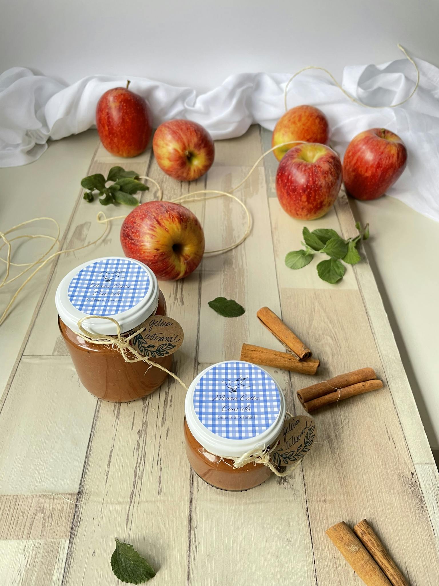 Jars of homemade apple cinnamon jam with fresh apples and cinnamon sticks on a wooden table.